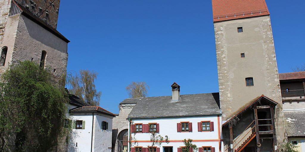 Bauernhof mit weißen Gebäuden, zwei Türmen und Gartenmöbeln unter blauem Himmel.